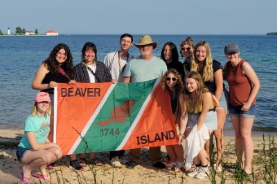 Students and professor standing on the Beaver Island shore, holding a flag, with Lake Michigan in the background